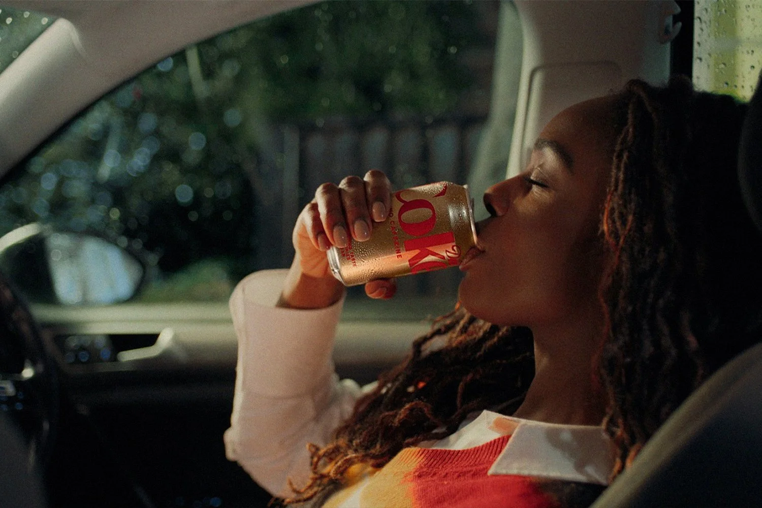 Film still: a woman pausing to drink a Diet Coke in a parked car.